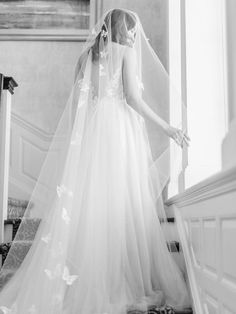 a woman in a wedding dress is walking down the stairs with her veil over her head