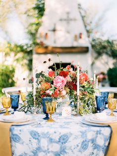 the table is set with blue and white dishes, candles, and flowers on it