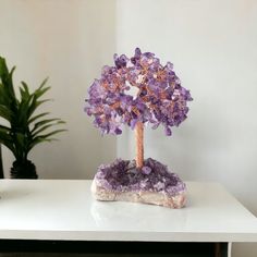 a small tree made out of amethyst crystals on a white table next to a potted plant