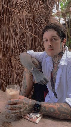 a tattooed man sitting at a table with a drink