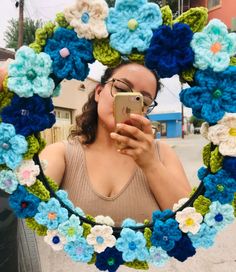 a woman taking a selfie in front of a crocheted wreath with flowers