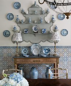 a dining room table with blue and white china on it's wall above a shelf