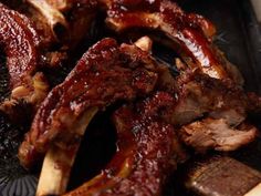 some ribs and other meats are on a black plate with chopping utensils