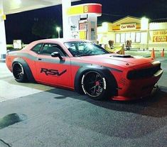 a red and gray car is parked in front of a gas station at night time