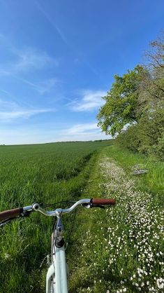 a bike parked on the side of a dirt road next to a lush green field