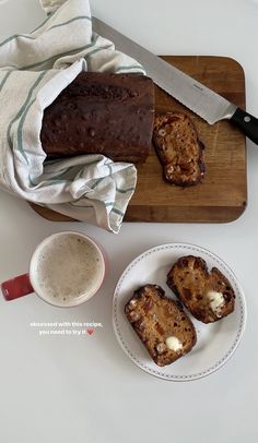 two pieces of bread on a cutting board next to a cup of coffee and a knife