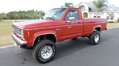 a red pick up truck parked on the side of a road in front of a house