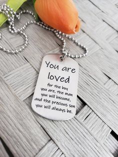 a dog tag with the words you are loved on it next to an orange flower