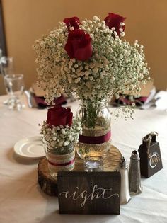 flowers in vases sitting on top of a wooden block at a wedding reception table