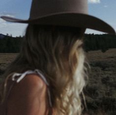 a woman wearing a cowboy hat standing in the middle of a field