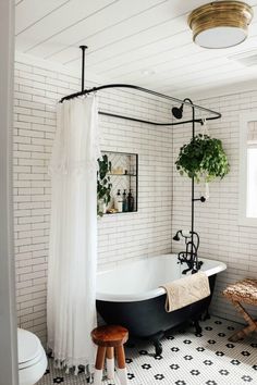 a black and white bathroom with a claw foot bathtub, shower curtain, stools and potted plants