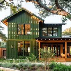 a green house with lots of windows and wood trimmings on the front porch