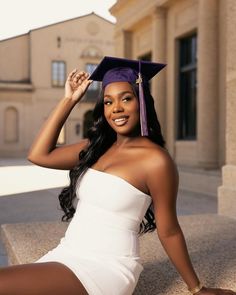 a woman in a graduation cap and gown sitting on the ground