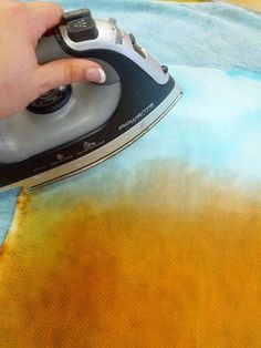 a person using an iron on top of a cloth with yellow and blue dyes