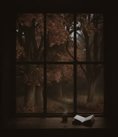 an open book sitting on top of a window sill next to a forest filled with trees