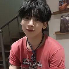 a young man with black hair wearing a red shirt and beaded necklace on his neck