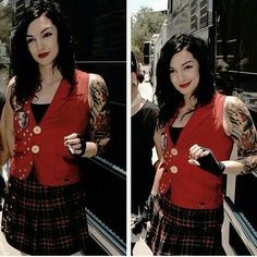 a woman in a red vest and plaid skirt with tattoos on her arms, holding a cell phone