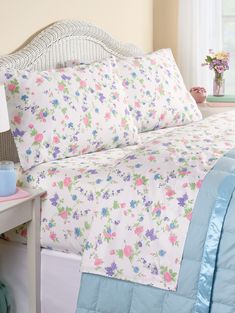 a bed with floral sheets and pillows in a small room next to a window,