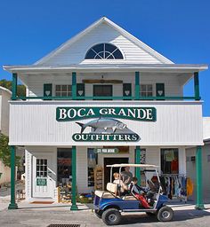 a golf cart is parked in front of a white building with green trim and the name boca grande outfitters on it