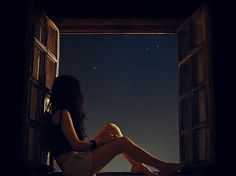 a woman sitting on the window sill looking out at the night sky and stars