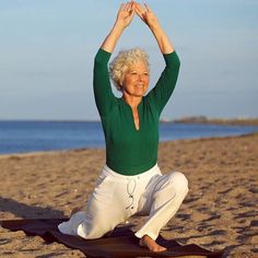 an older woman is doing yoga on the beach