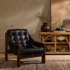 a black chair sitting in front of a wooden table with a vase on top of it