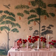 a table with flowers and candles on it in front of a wall painted with trees