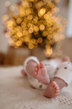 a baby laying on top of a bed next to a christmas tree with lights in the background