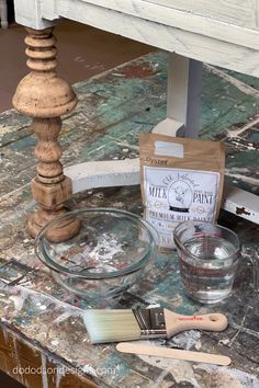 a table with paint, brushes and other items sitting on top of it next to a wooden stand