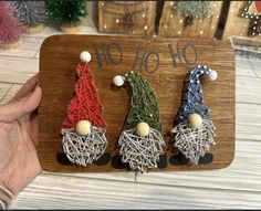 three gnomes made out of string on a wooden board with christmas decorations in the background