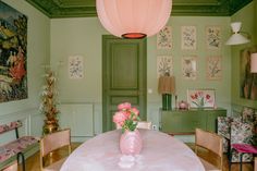 a pink vase with flowers sitting on top of a table in a room filled with pictures