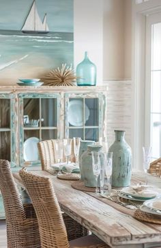 a dining room table set with plates, glasses and vases in front of a painting on the wall