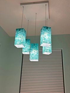 four lights hanging from a ceiling in a room with blinds on the window sill