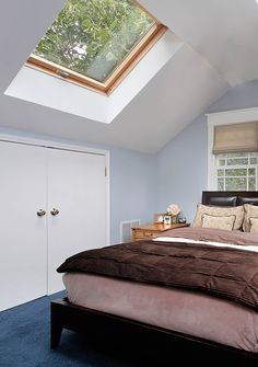 a large bed sitting under a skylight in a bedroom next to a dresser and window