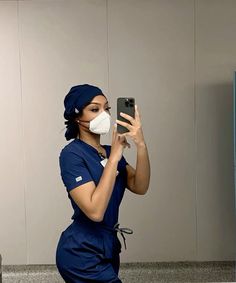 a woman in scrubs is taking a selfie with her cell phone while wearing a surgical mask