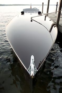 the front end of a black boat docked at a dock with water in the background