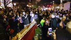 a crowd of people standing around each other in front of a building with christmas lights on it