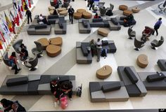 many people are walking around in an airport with couches and tables on the floor