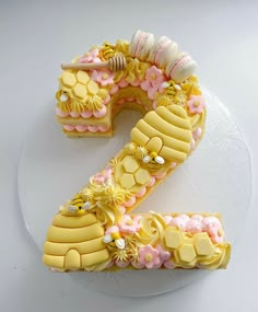 a cake shaped like the number two on top of a white plate with pink and yellow decorations