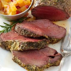 some meat is sitting on a plate next to a bowl of vegetables and a fork