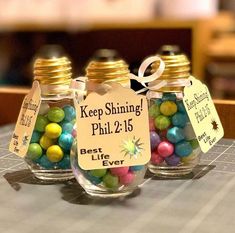 three small glass jars filled with colorful candies on top of a wooden table next to a sign that says keep shining phil 2 15 best life ever