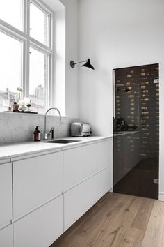 a kitchen with white cabinets and wood flooring in front of a window that is open to the outside