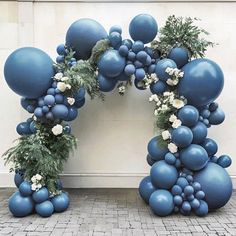 an arch made out of blue balloons and greenery with white flowers on the top