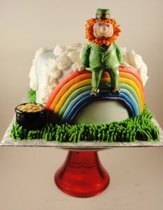 a cake with a leprechaun sitting on top of it and rainbow in the background