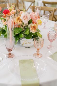 the table is set with pink and orange flowers, candles, napkins, and wine glasses