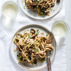 two plates of pasta with mushrooms, peas and parsley on a white tablecloth