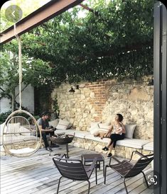 two people sitting on the back deck of a house with a hammock hanging from it's roof