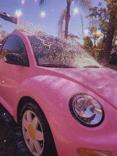 a pink car is parked in front of a palm tree and has water sprinkles all over it