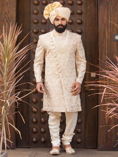 a man standing in front of a wooden door wearing a white suit and turban