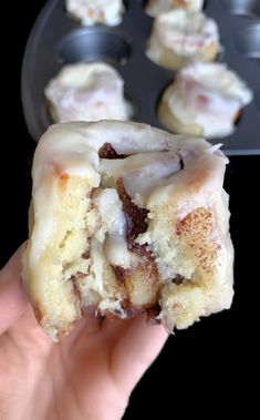 a hand holding a half eaten doughnut in front of other pastries on a pan